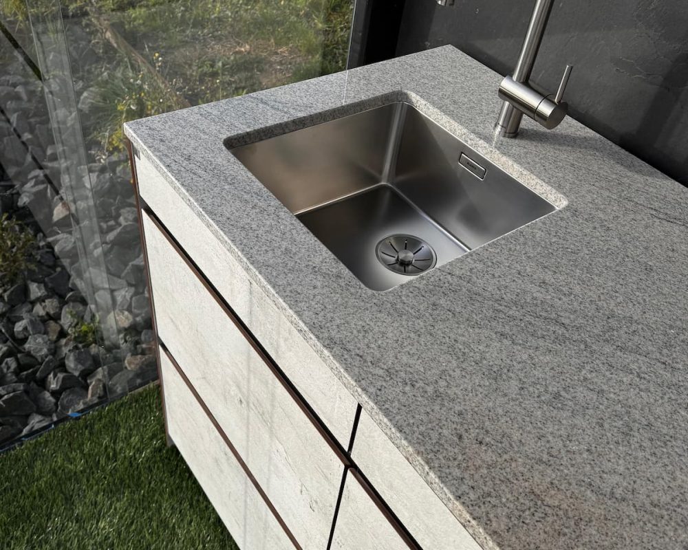Detail der Naturstein-Arbeitsplatte mit Edelstahlspüle und Armatur an der Abverkauf-Outdoorküche.